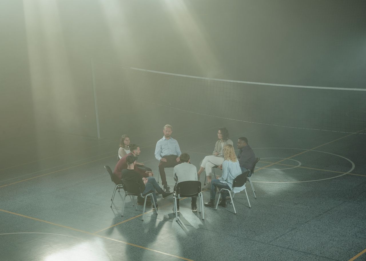 A diverse group gathering in a gym for a supportive therapy session, with sunlight streaming through the haze.
